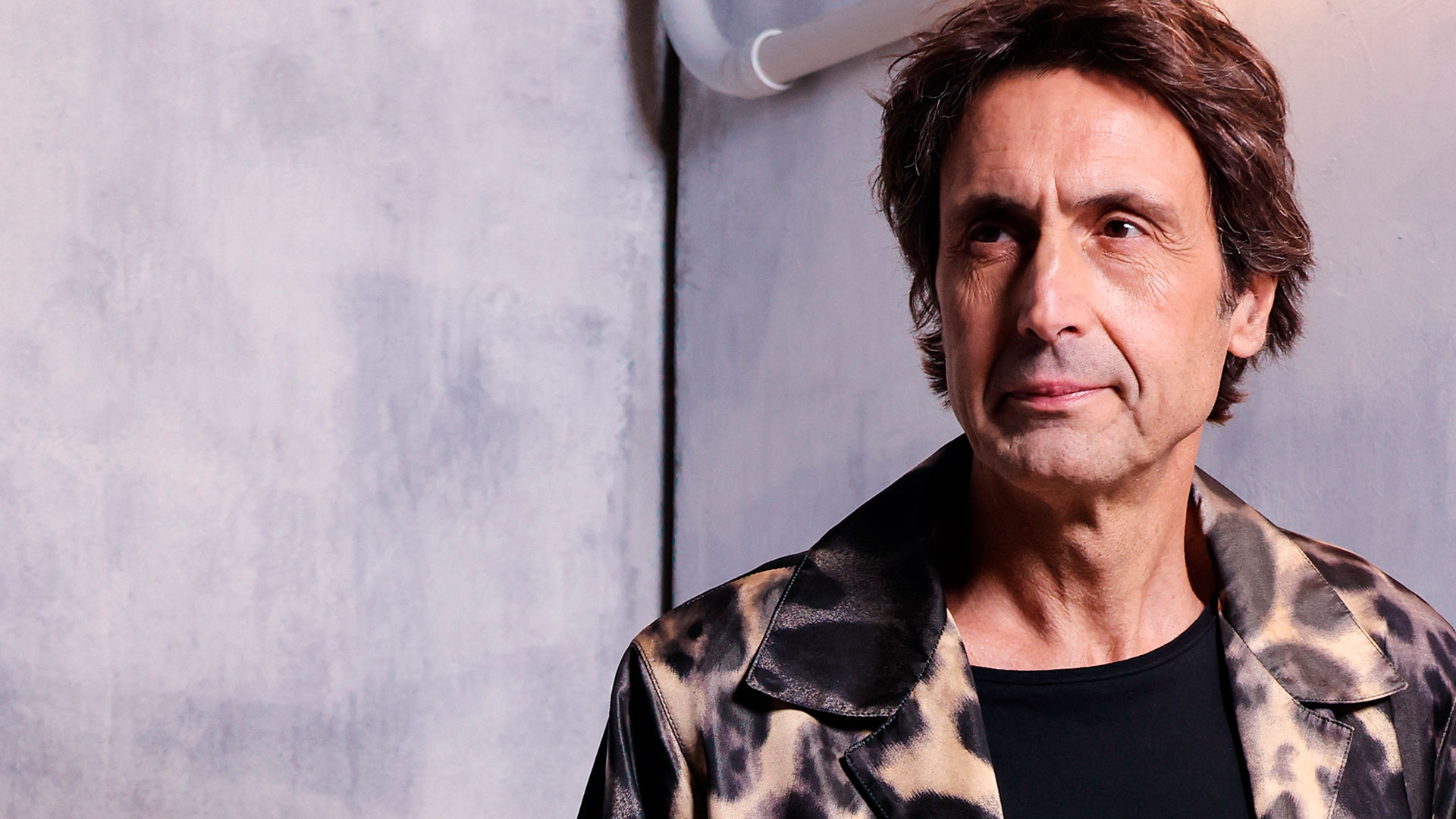 Francesco David Clemente with a confident smile and determined gaze, looking into the distance; color portrait with minimalist industrial background and designer clothing.